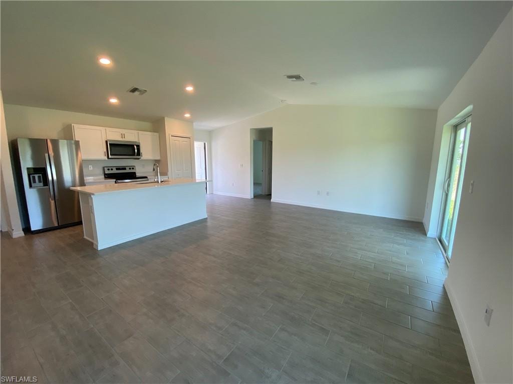 Kitchen featuring a center island with sink, sink, lofted ceiling, white cabinetry, and appliances with stainless steel finishes