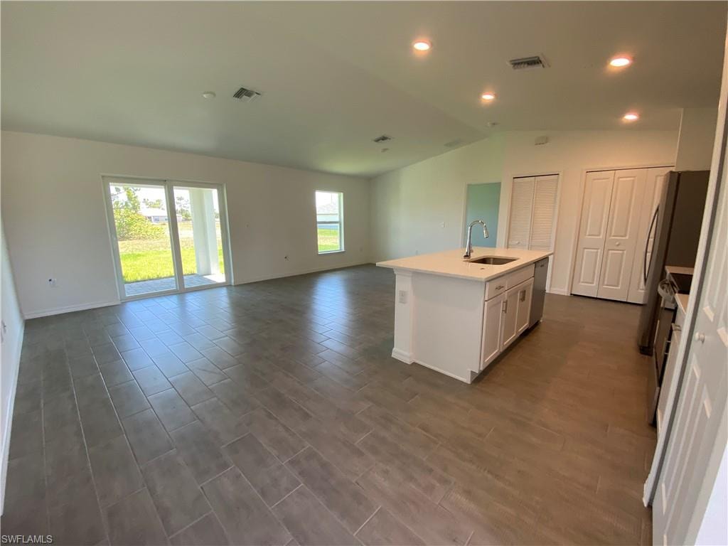 Kitchen featuring a kitchen island with sink, stainless steel dishwasher, white cabinets, sink, and lofted ceiling