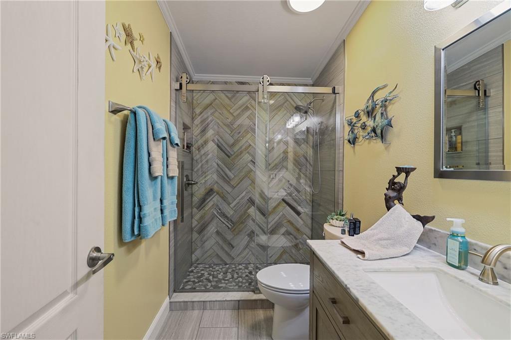 Bathroom featuring a glass-enclosed shower with herringbone tile surround and river rock floor, a single vanity with stone countertop, and wood-finish flooring