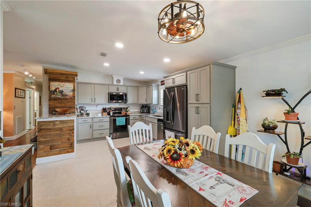 Open-concept kitchen and dining area featuring light gray cabinetry, stainless steel appliances, a center island with wood-finish paneling, recessed lighting, and a decorative ceiling fan