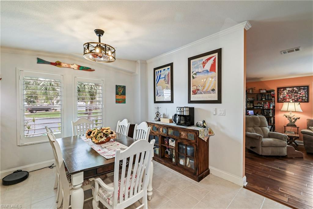 Dining area featuring white plantation shutters, a decorative ceiling light fixture, crown molding, and tiled flooring