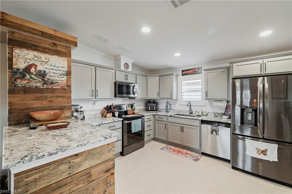 Kitchen featuring light gray cabinetry, stainless steel appliances, granite countertops, and wood-finish accent paneling