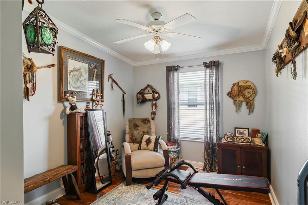 Interior room featuring crown molding, a ceiling fan with light fixture, wood-finish flooring, and a window with blinds and sheer curtains