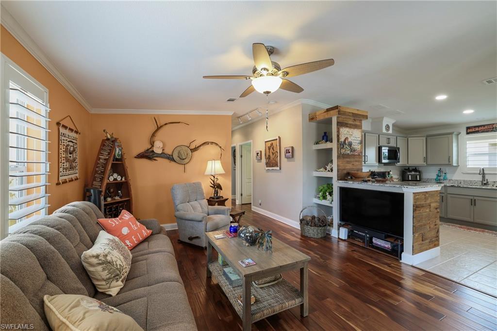 Open-concept living space featuring wood-finish flooring, a ceiling fan, and crown molding