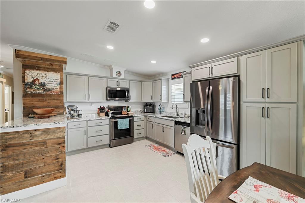 Kitchen featuring light grey cabinetry with brushed nickel hardware, white quartz countertops, stainless steel appliances, and a wood-finish accent wall