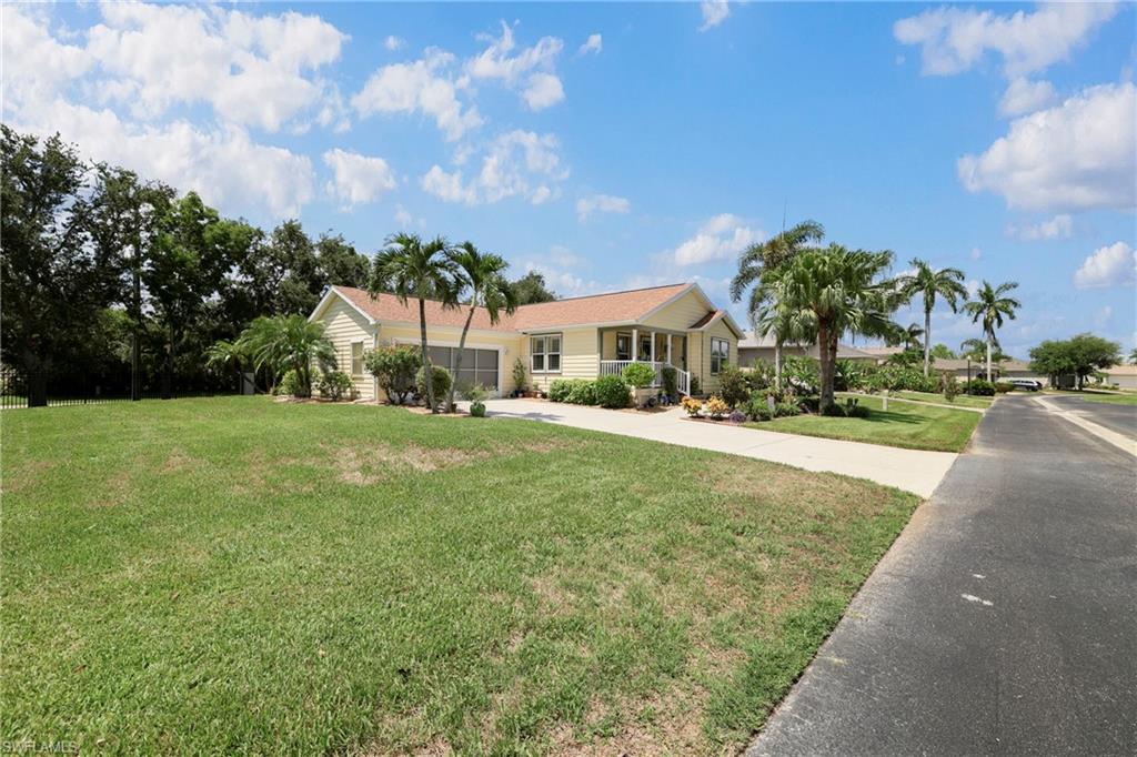 Spacious property featuring a light yellow exterior with a covered front porch, a paved driveway, and mature palm trees