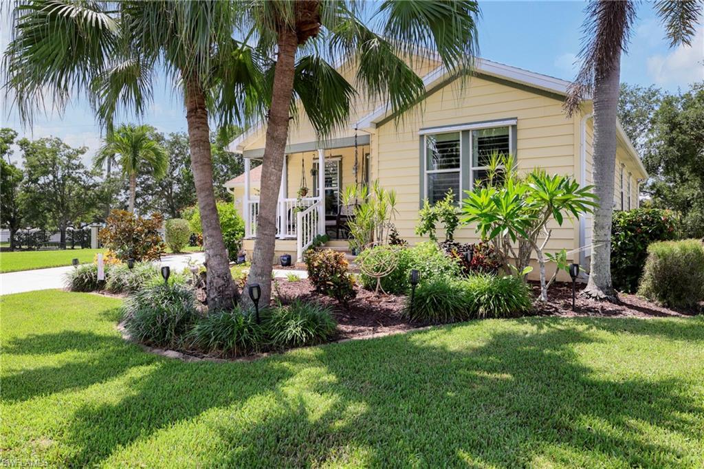 Yellow exterior siding with white trim, featuring a front porch with white railings, a large front window with louvered shutters, and mature palm trees