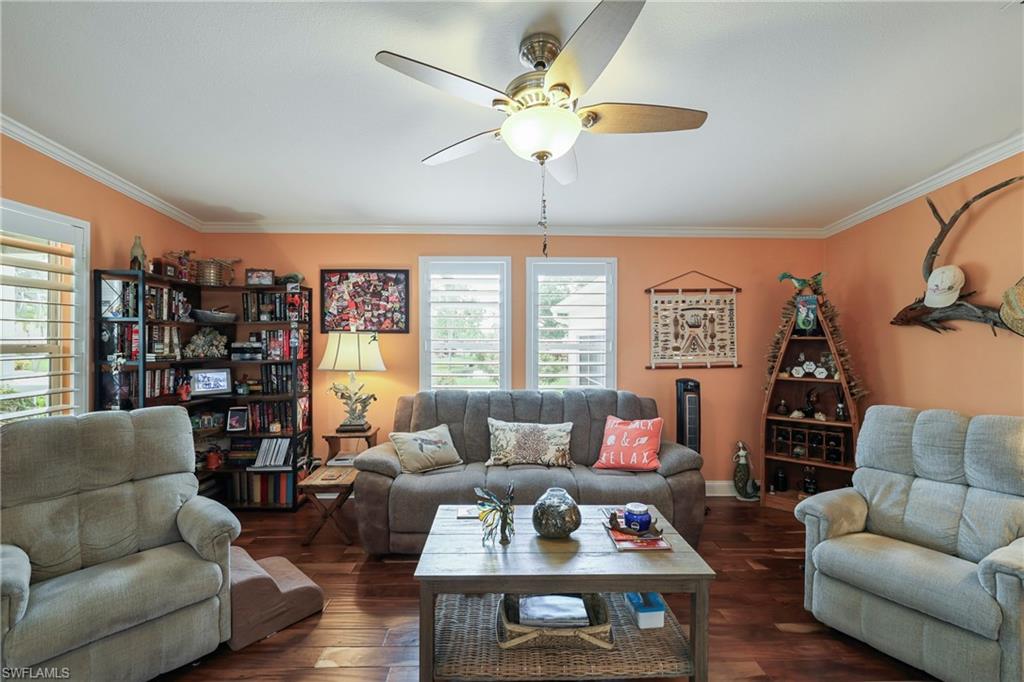 Living space featuring hardwood flooring, crown molding, a ceiling fan with integrated lighting, and multiple windows with plantation shutters