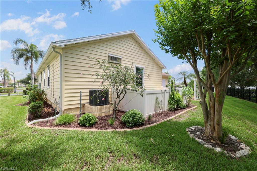 Exterior siding with white trim, featuring an established tree and landscaped shrubbery