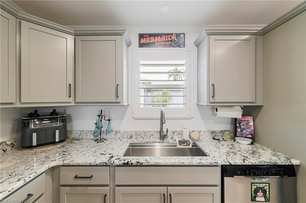 Kitchen featuring light gray shaker-style cabinetry with dark hardware, granite-style countertops, an undermount stainless steel sink with a gooseneck faucet, a window with plantation shutters, and a stainless steel dishwasher
