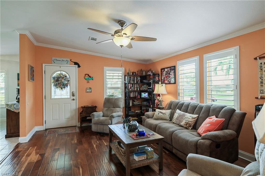 Living area featuring wood-finish flooring, white crown molding, and a ceiling fan with integrated lighting