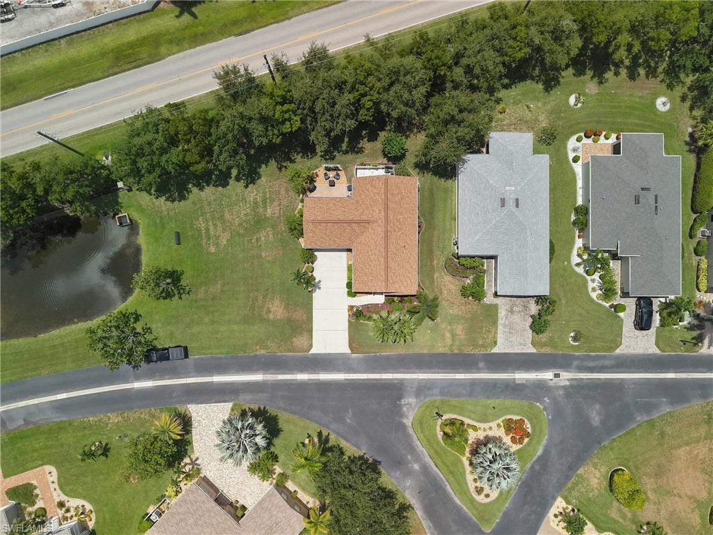 Aerial perspective showcasing a property with a brown shingle roof, a light-colored driveway, and a paved patio area