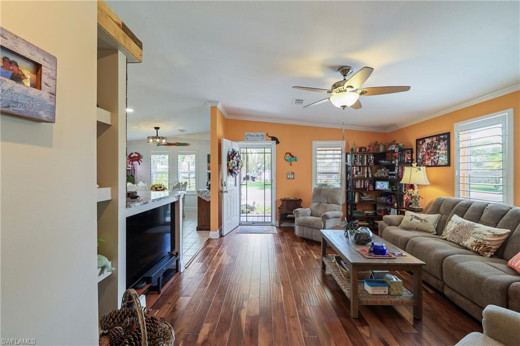 Spacious living area featuring wood-finish flooring, a ceiling fan with integrated lighting, and multiple windows with plantation shutters