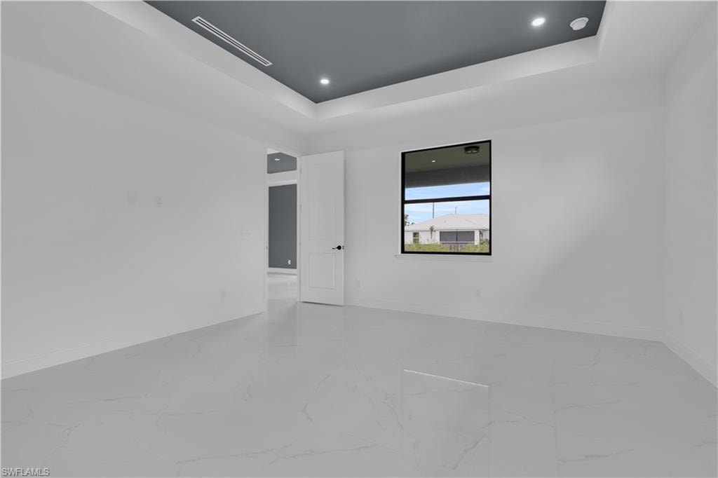 Spacious interior room featuring a tray ceiling with recessed lighting, large window with black framing, white panel door, and light-toned tile flooring