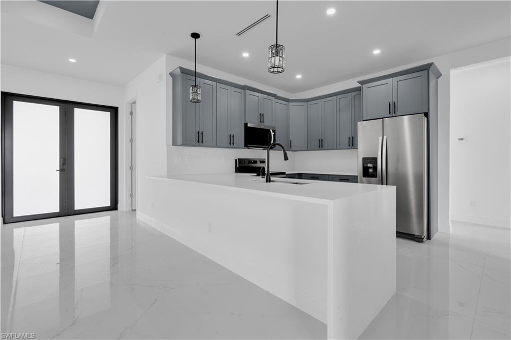 Modern kitchen featuring light gray cabinetry, stainless steel appliances, a center island with a white countertop, and white tile flooring