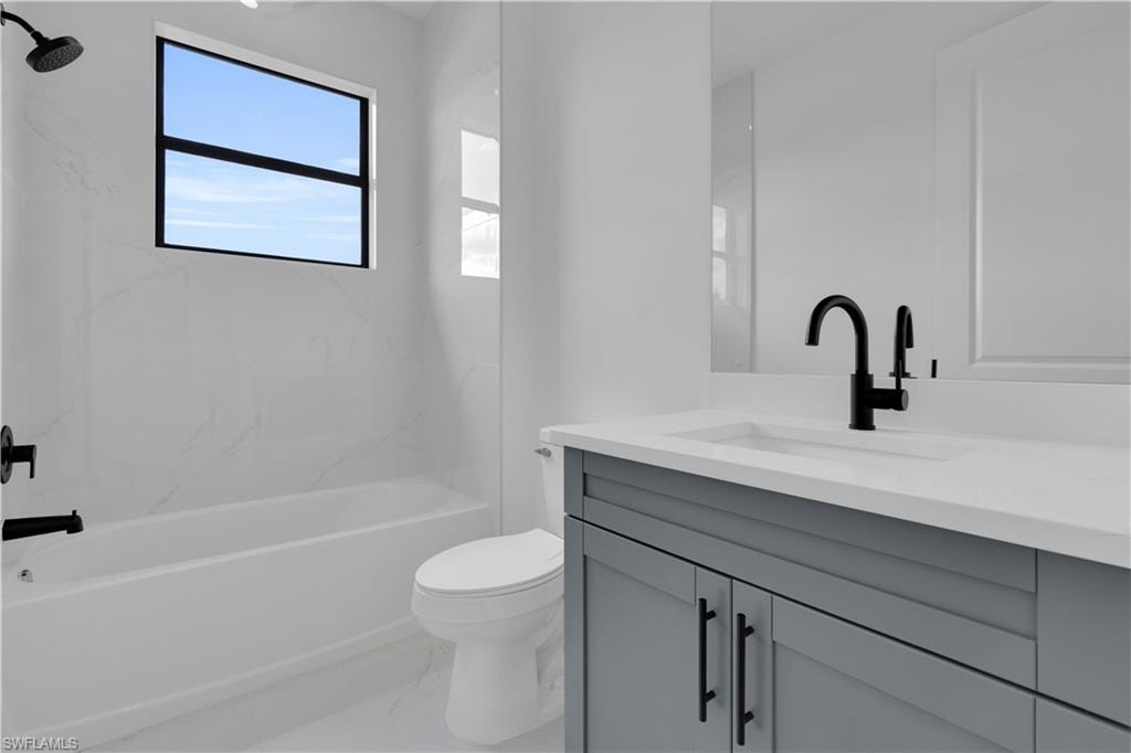 Bathroom featuring a tub/shower combination with black fixtures, a window above the tub, a white toilet, a gray vanity with a white countertop, and a black faucet