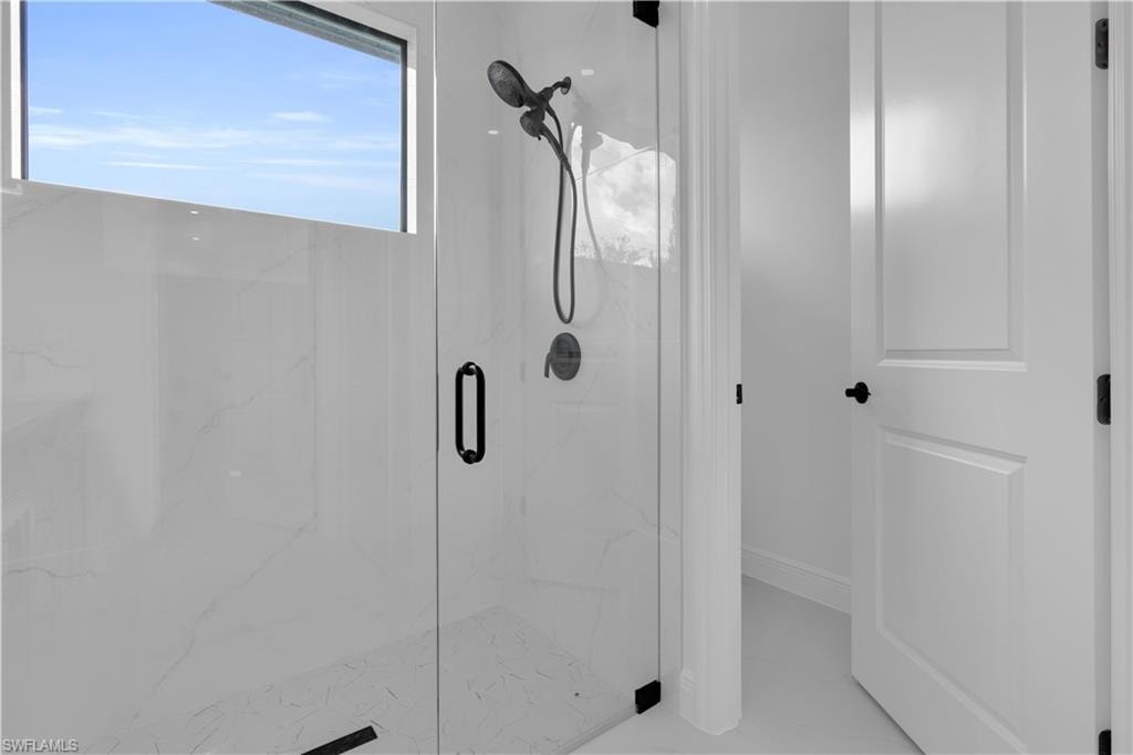 Spacious shower with a glass enclosure, a matte black shower system, and white marble-look wall tiles