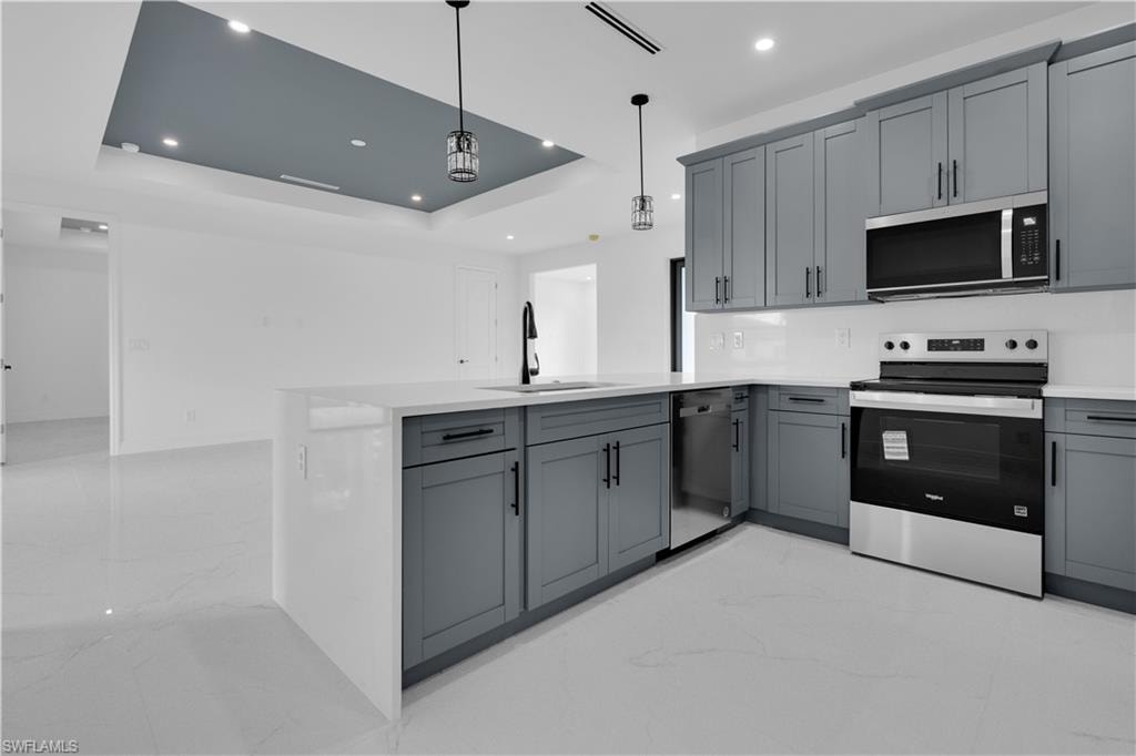 Modern kitchen featuring sleek gray cabinetry, stainless steel appliances, white countertops, and a waterfall island with an undermount sink
