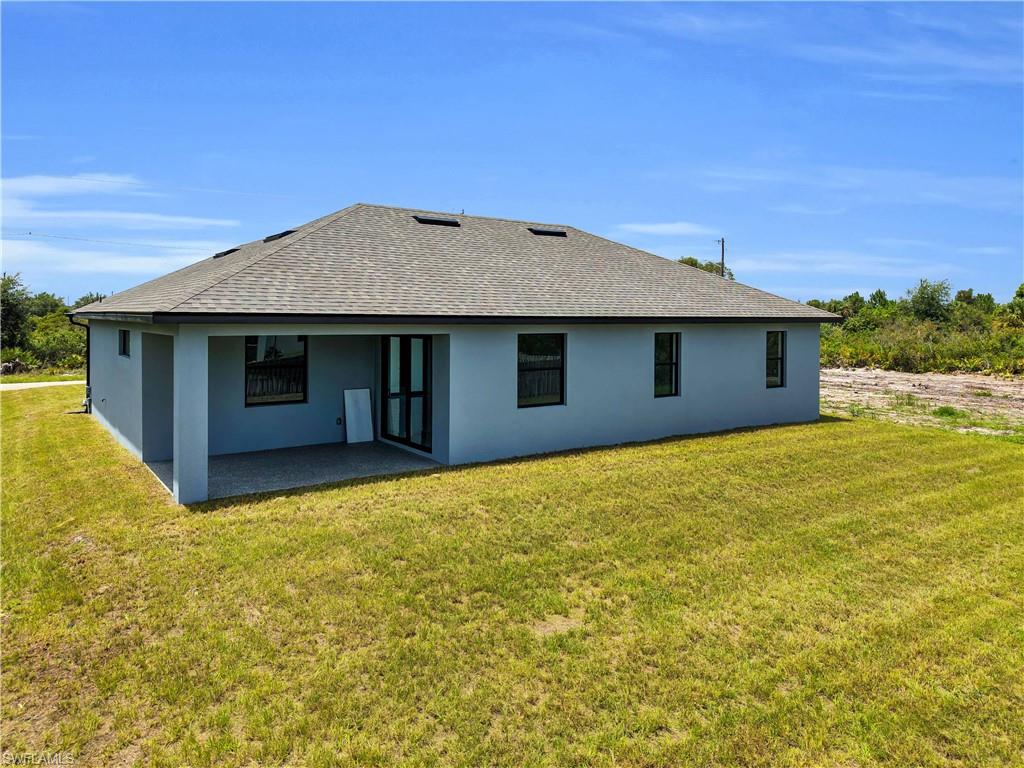 Contemporary single-story residence featuring a gray exterior finish, a covered patio with concrete flooring, a dark composition shingle roof, and multiple dark-framed windows