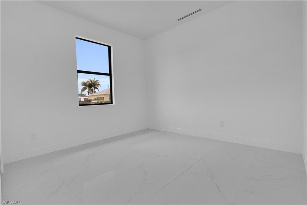 Spacious room featuring white walls, white baseboards, and large format light-toned tile flooring
