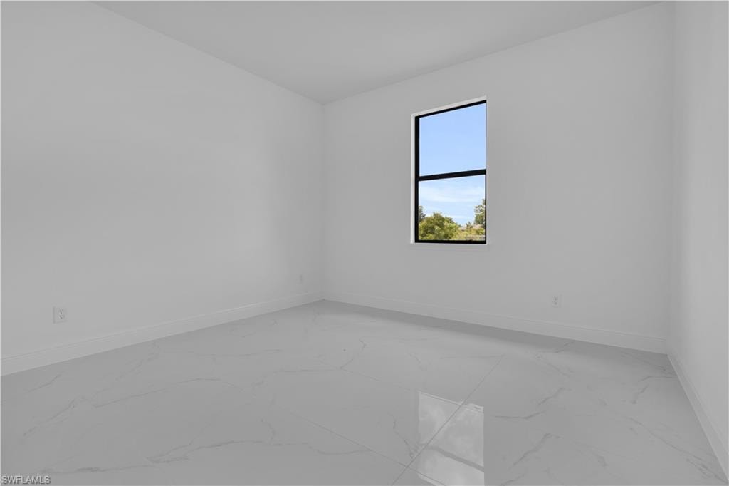 Bright interior space featuring a single window with black trim, white walls, white baseboards, and large format white tile flooring with subtle veining