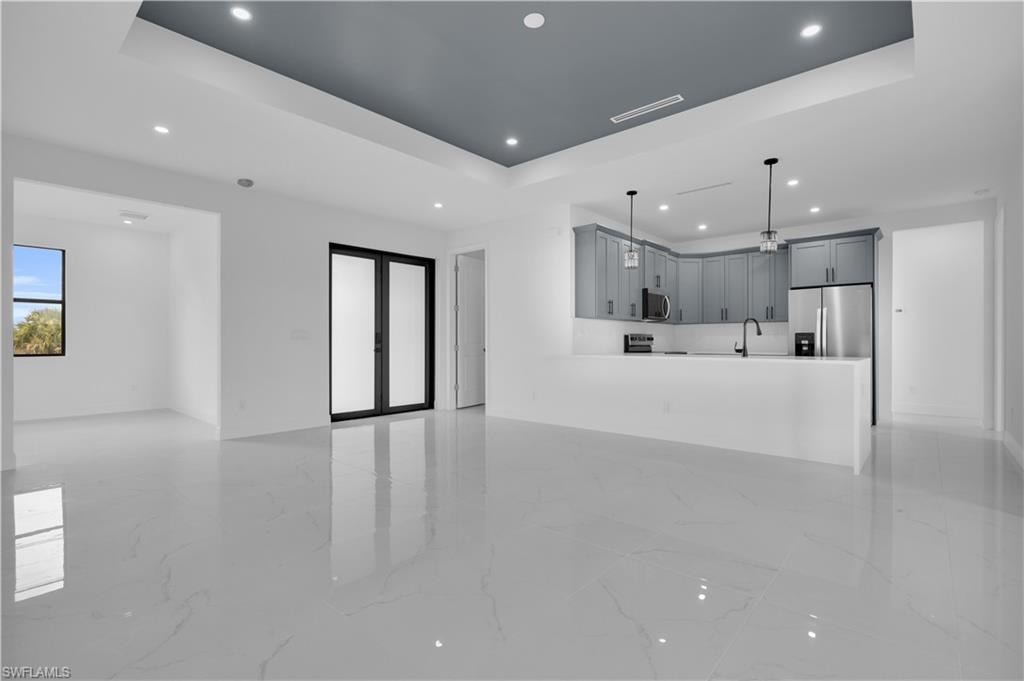 Open-concept living space featuring high-gloss tile flooring, a tray ceiling with recessed lighting, and a modern kitchen with grey cabinetry, stainless steel appliances, and a breakfast bar