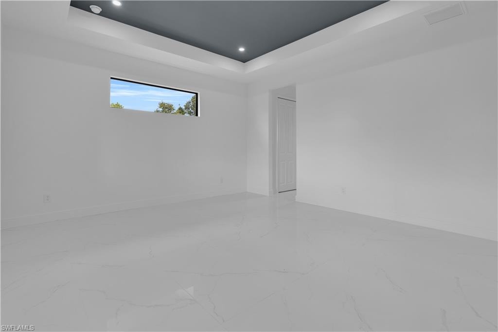 Spacious room featuring white tile flooring, a painted tray ceiling, recessed lighting, and a horizontal window