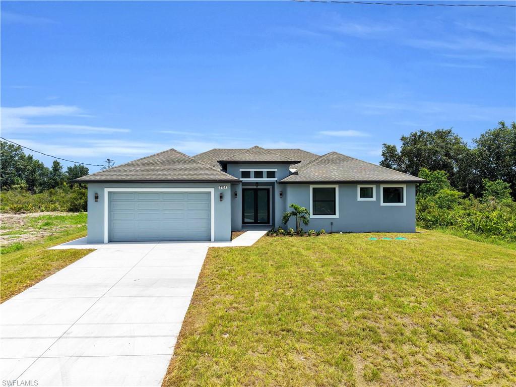 Contemporary home with a light blue exterior, dark shingle roof, a two-car garage, concrete driveway, and a front entry with vertical windows