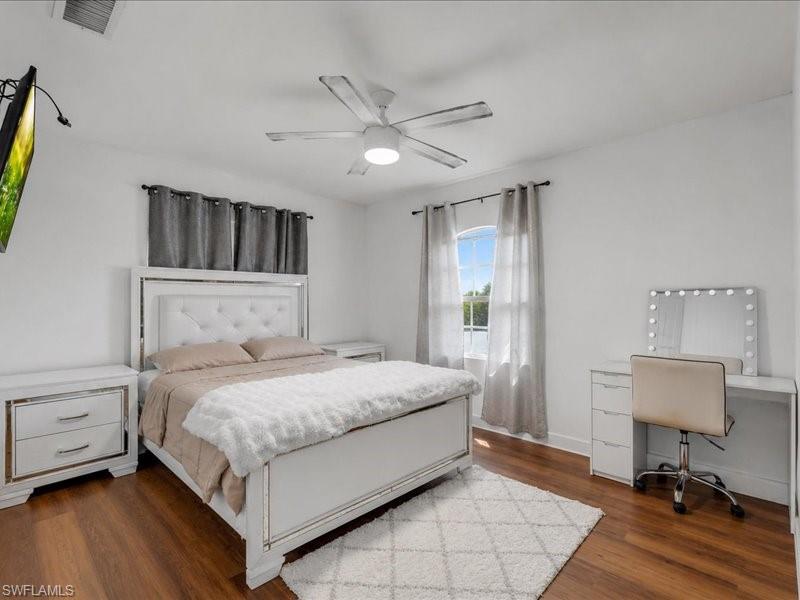 Spacious bedroom featuring wood-finish flooring, a ceiling fan with integrated lighting, and a large window with sheer and blackout curtain options