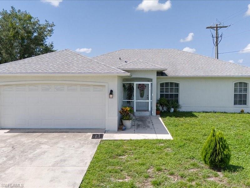 Single-story residence featuring a two-car garage with a paneled door, a screened front entryway, arched windows, and a paved driveway
