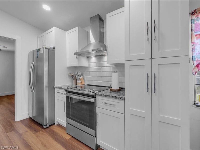 Kitchen featuring white shaker-style cabinetry, granite countertops, stainless steel appliances, subway tile backsplash, and wood-finish flooring