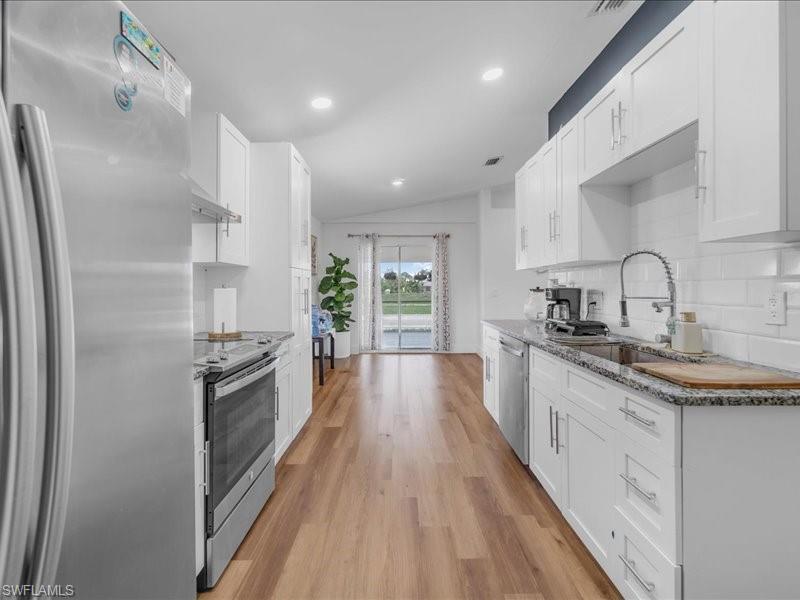 Kitchen featuring white shaker cabinetry, granite-style countertops, stainless steel appliances, wood-finish flooring, and recessed lighting