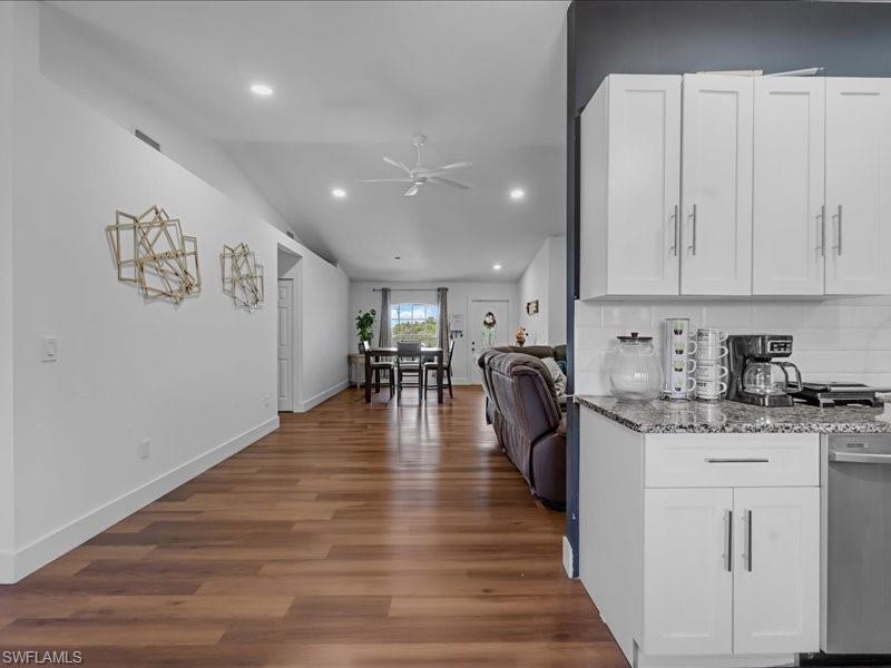 Open-concept living area featuring wood-finish flooring, recessed lighting, and a kitchen with white shaker cabinetry, light-toned countertops, and a subway tile backsplash