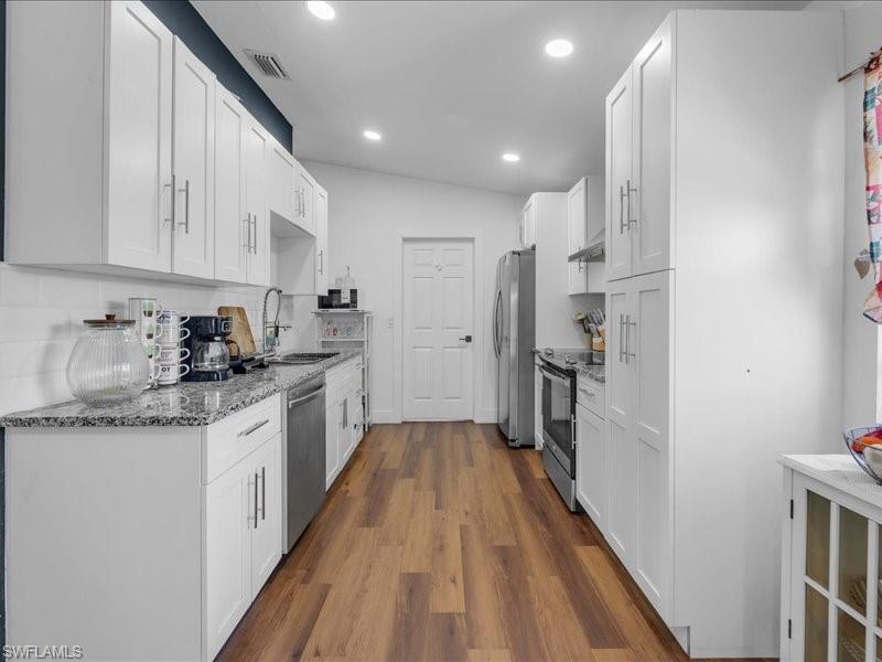 Galley-style kitchen featuring wood-finish flooring, white cabinetry, integrated stainless steel appliances, speckled countertops, and recessed lighting