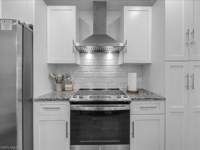 Stainless steel range with coordinating ventilation hood, white shaker-style cabinetry, subway tile backsplash, and granite countertops