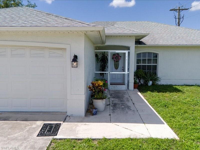 White stucco exterior featuring a screened front entry, arched front window, concrete walkway, and a two-car garage