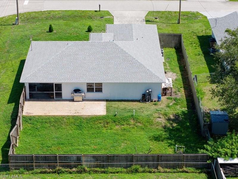 Rear exterior featuring a screened patio, expansive grassed yard, wood fencing, and a utility shed