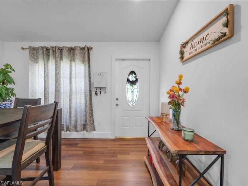 Entryway featuring a white door with decorative glass, wood-finish flooring, and a window with drapes