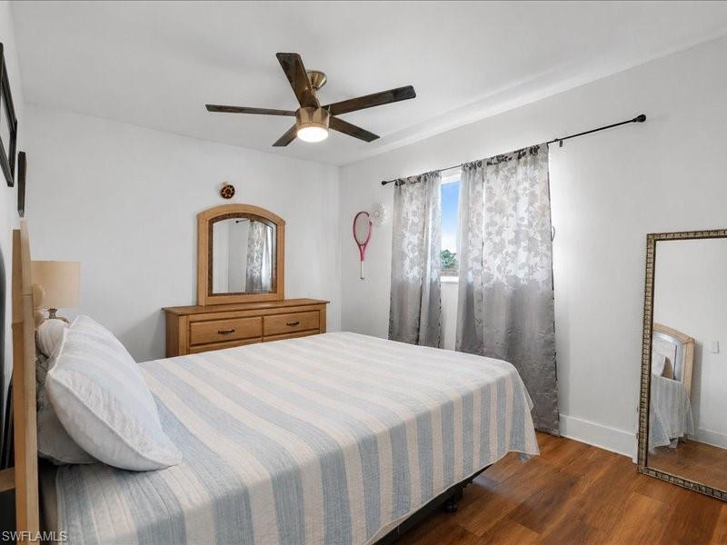 Bedroom featuring wood-finish flooring, a ceiling fan with integrated lighting, and a window with a curtain rod
