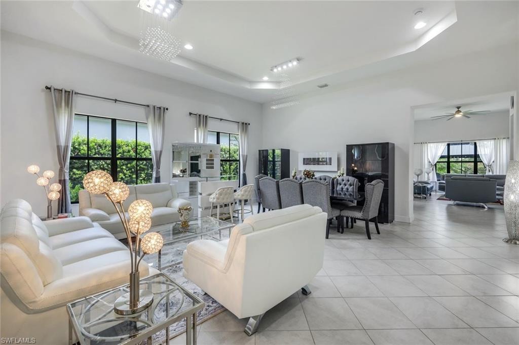 Spacious living area featuring large format tile flooring, multiple recessed light fixtures, tray ceilings, and an integrated wet bar with seating