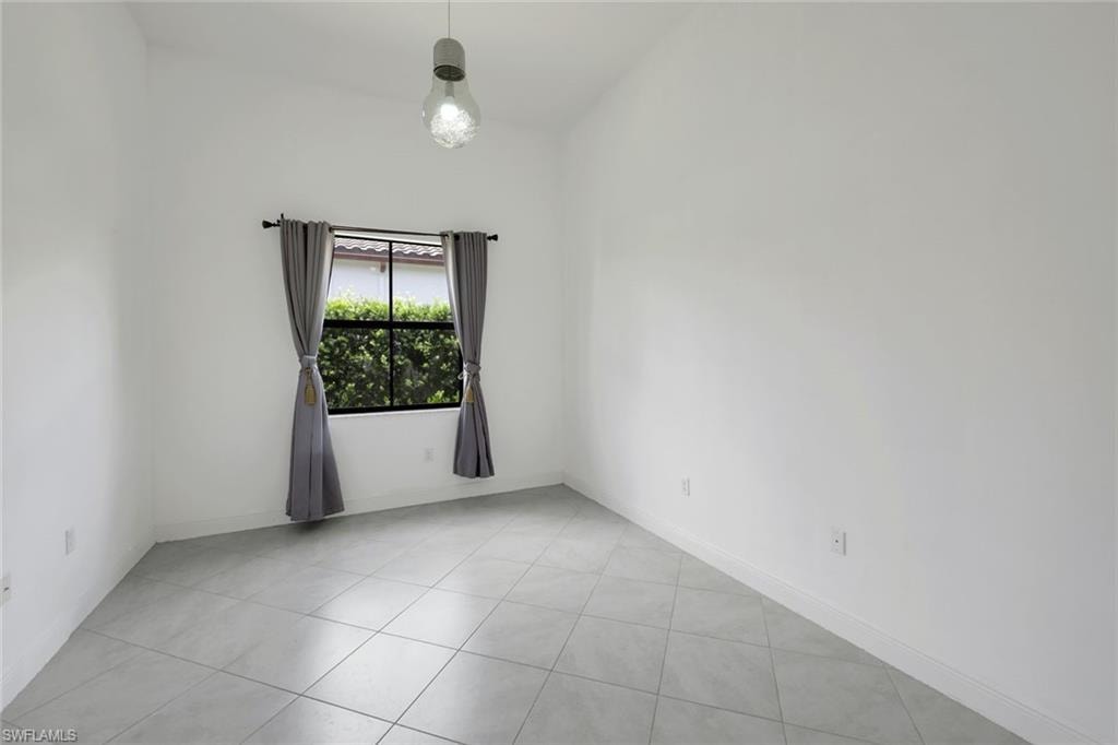 Expansive interior room featuring crisp white walls, large format tile flooring, a prominent window with exterior landscaping, a contemporary pendant light fixture, and high ceilings