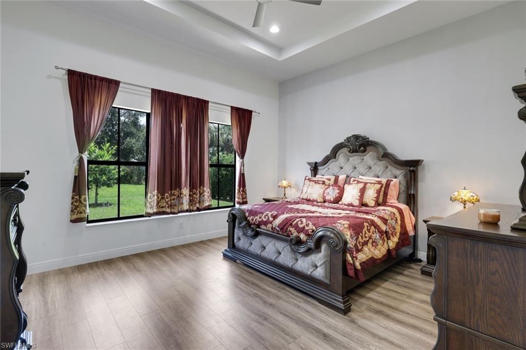 Recessed ceiling with a fan, wood-finish flooring, and a large window overlooking a green landscape