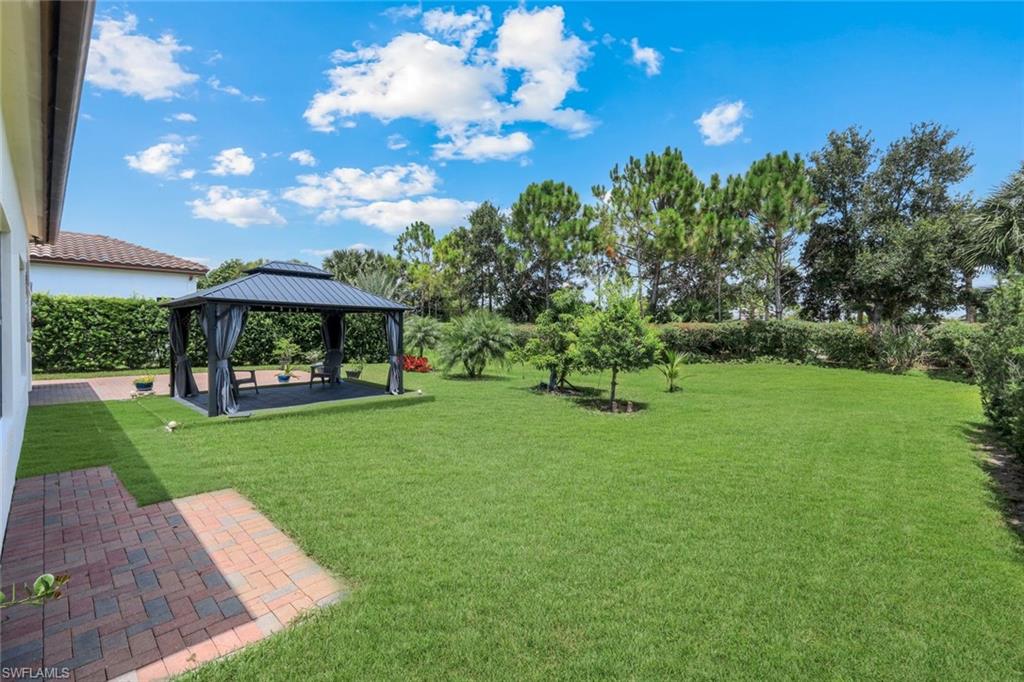Expansive green lawn with a covered gazebo, mature perimeter trees, shrubbery, and a brick paver patio