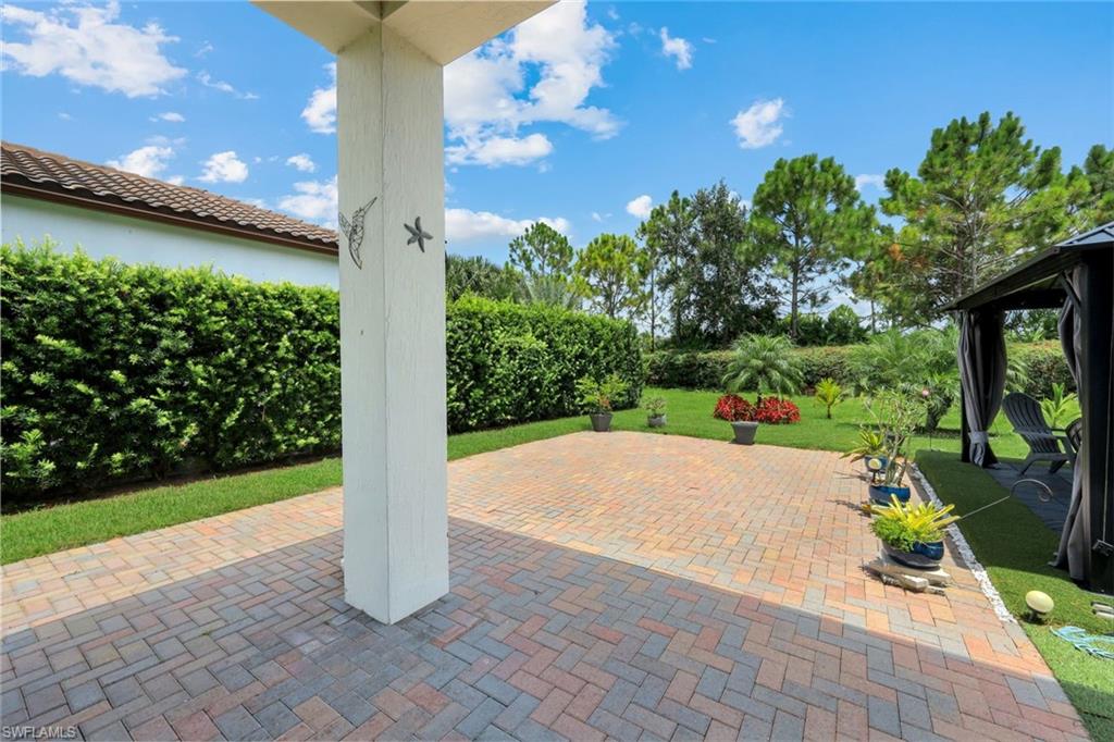 Expansive paver patio with a white structural column, bordered by manicured lawn and mature hedges