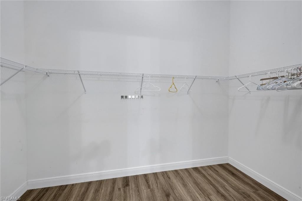 Spacious walk-in closet featuring white wire shelving, expansive wall space, wood-finish flooring, and crisp white baseboards