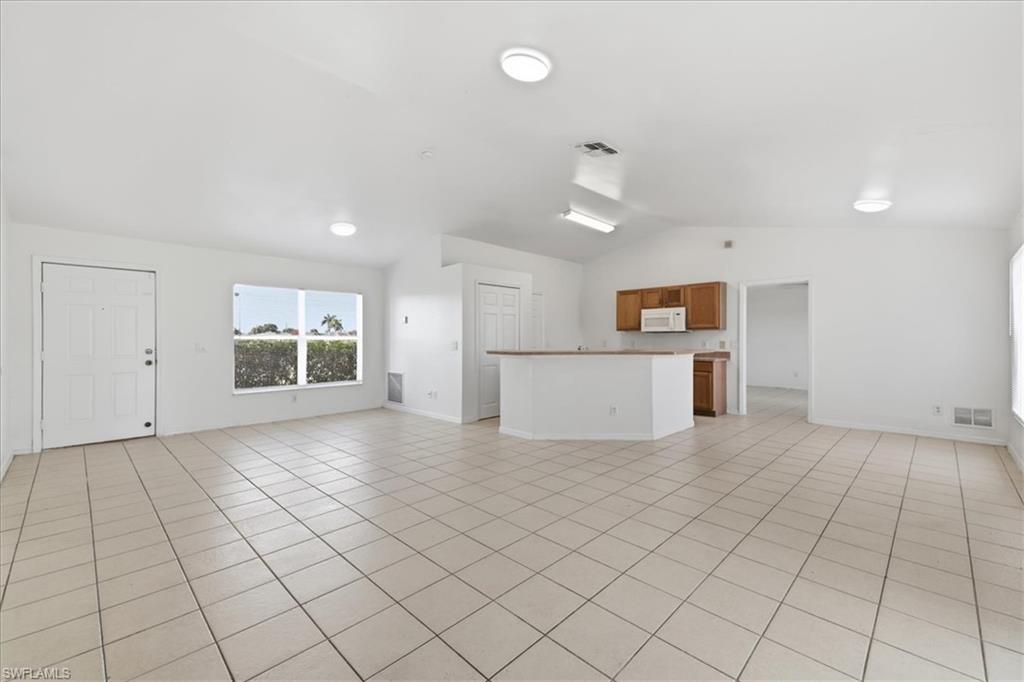 Spacious open-concept living area featuring light-toned tile flooring, vaulted ceilings, and recessed lighting