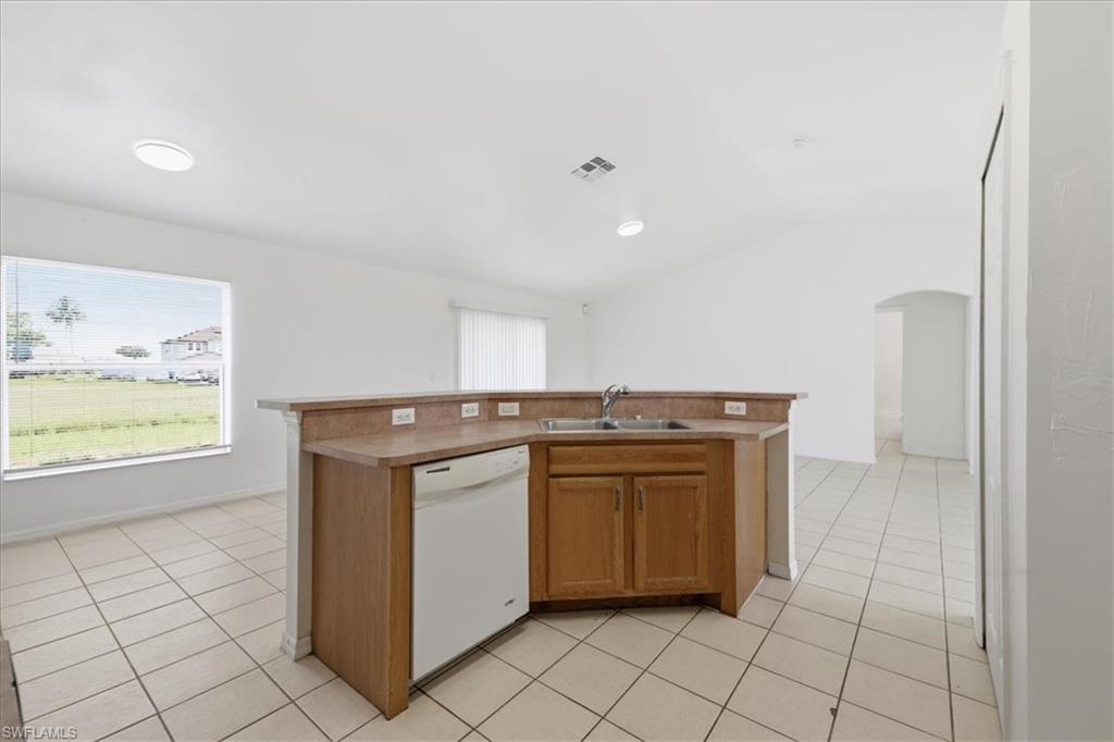 Kitchen featuring a peninsula with a double basin sink, wood-finish cabinetry, and a light-toned countertop