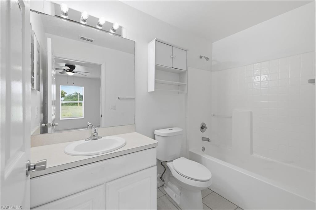 Bathroom featuring a white vanity with an integrated sink, a large wall-mounted mirror, overhead vanity lighting, a white toilet, and a combination tub/shower with white subway tile surround