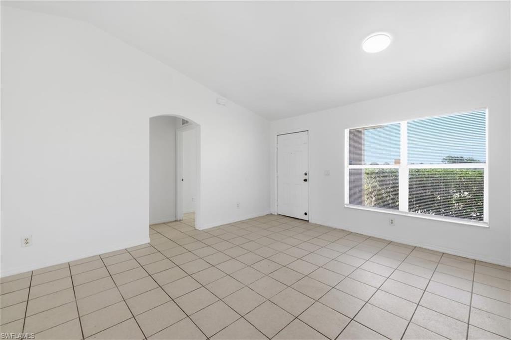 Spacious room featuring neutral tile flooring, a large window with blinds, and an arched entryway
