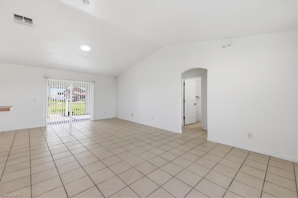 Spacious room featuring tile flooring, vaulted ceiling, and sliding glass doors with vertical blinds